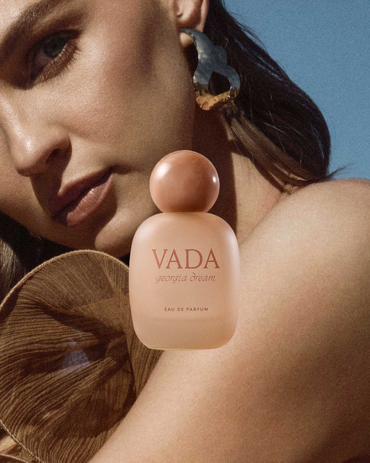 Perfume bottle labeled 'VADA' held by a person against a blue background
