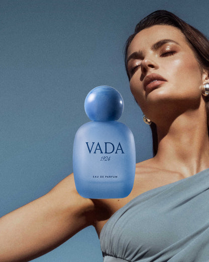 Woman holding a blue VADA perfume bottle against a clear blue sky