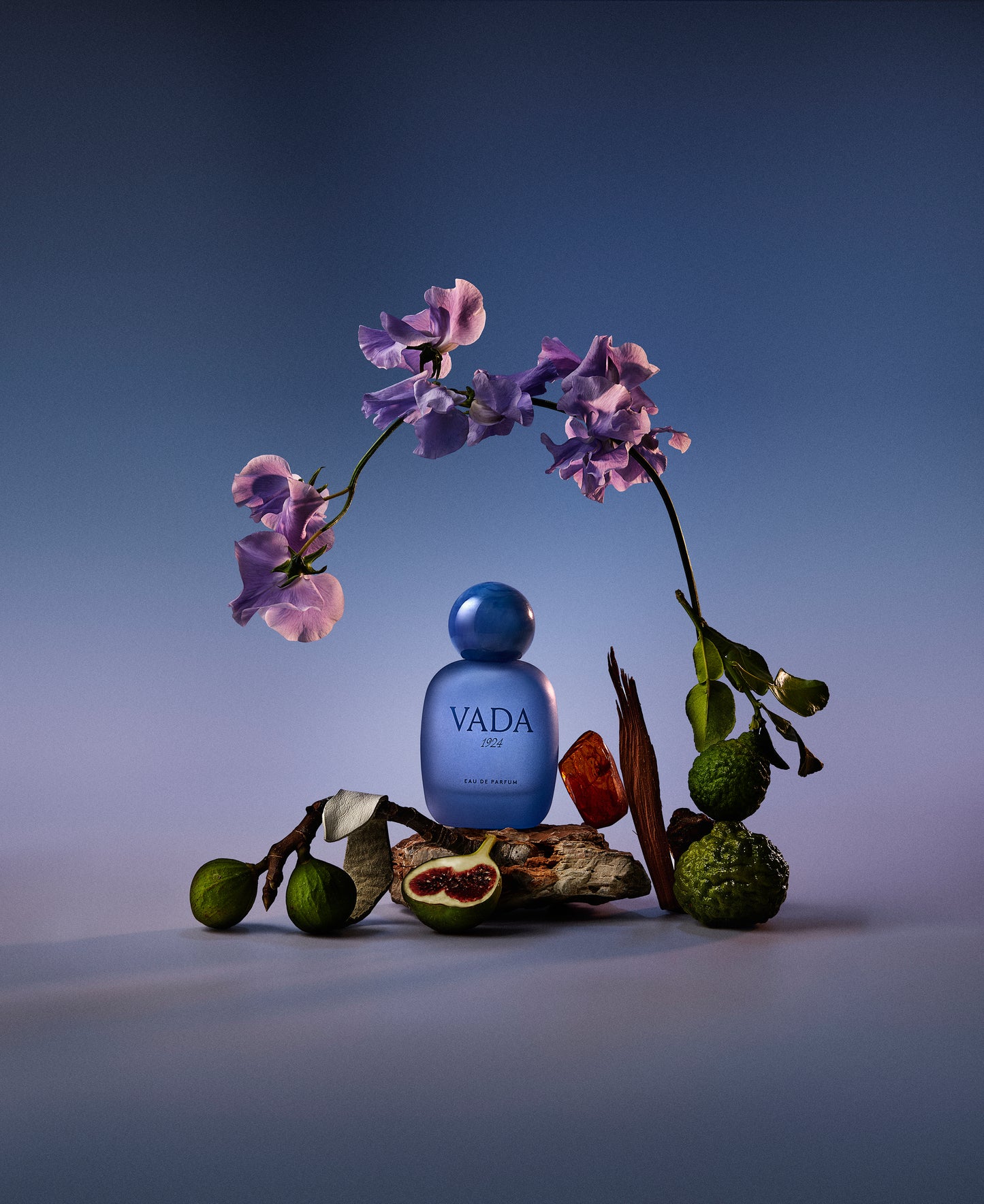 Blue VADA perfume bottle with flowers and fruits on a gradient background