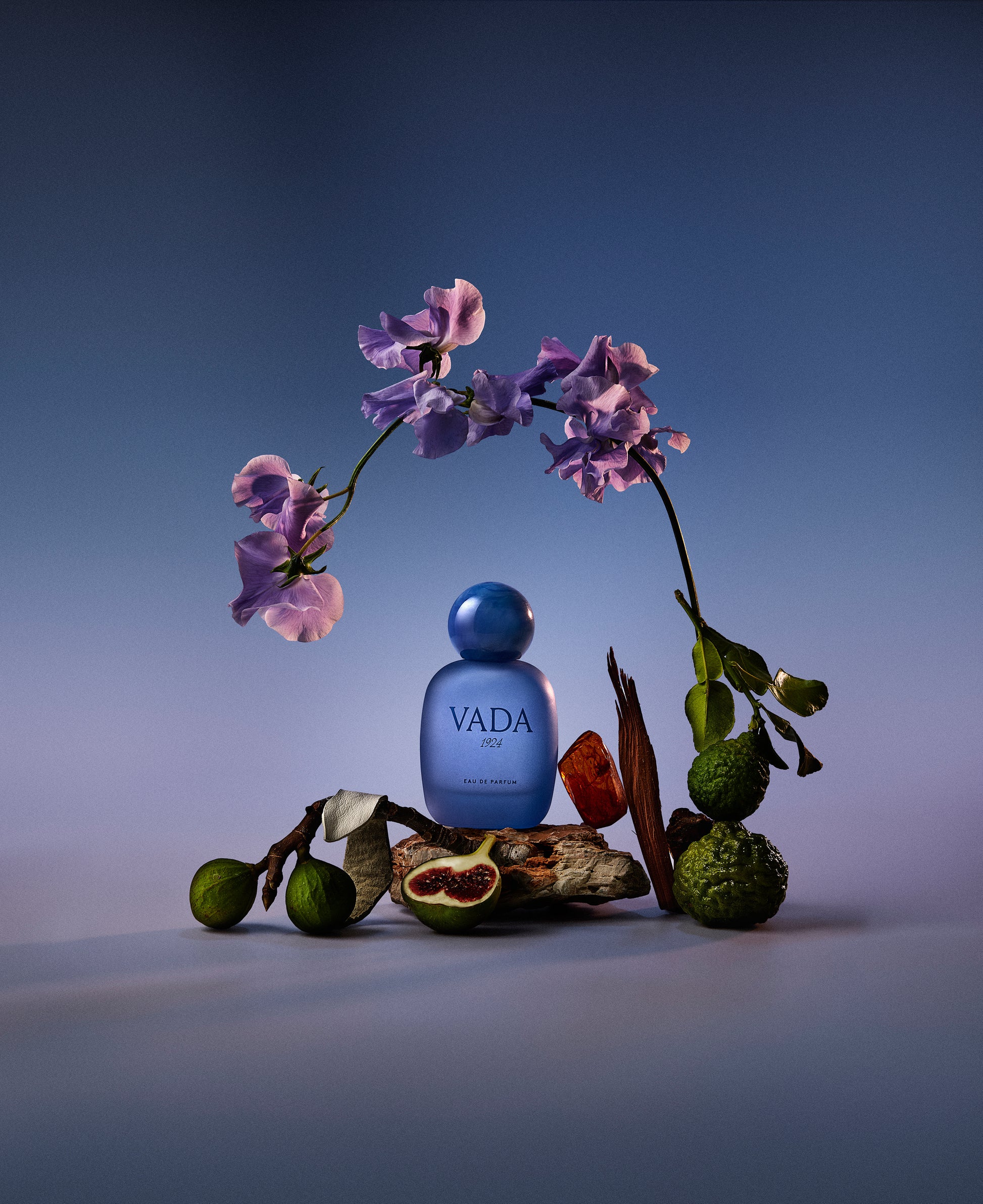 Blue VADA perfume bottle with flowers and fruits on a gradient background