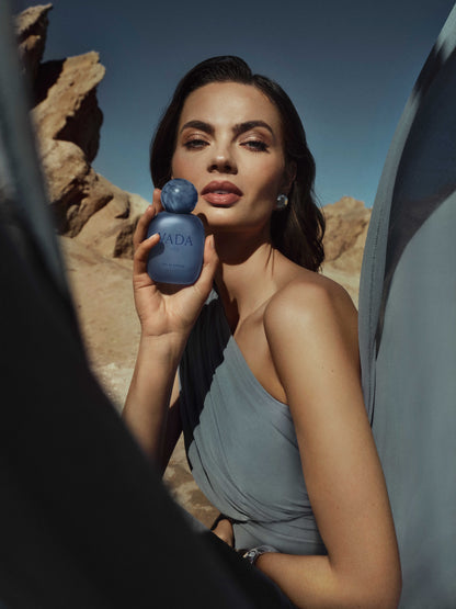 Woman holding a blue Vada perfume bottle in a desert setting