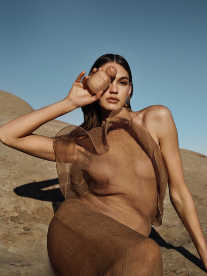 Woman holding a brown perfume bottle against a clear blue sky