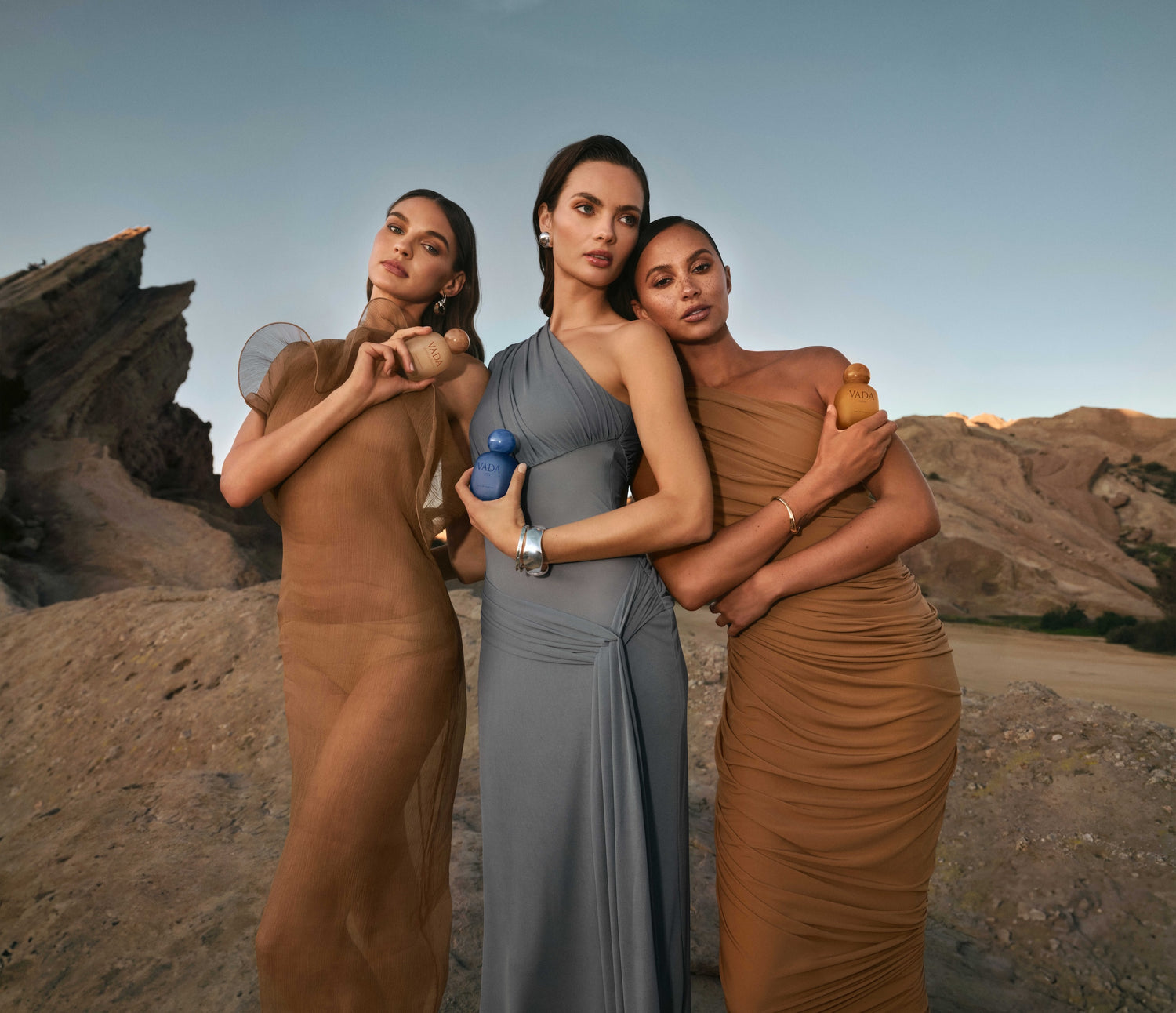 Three women in elegant dresses standing in a desert landscape