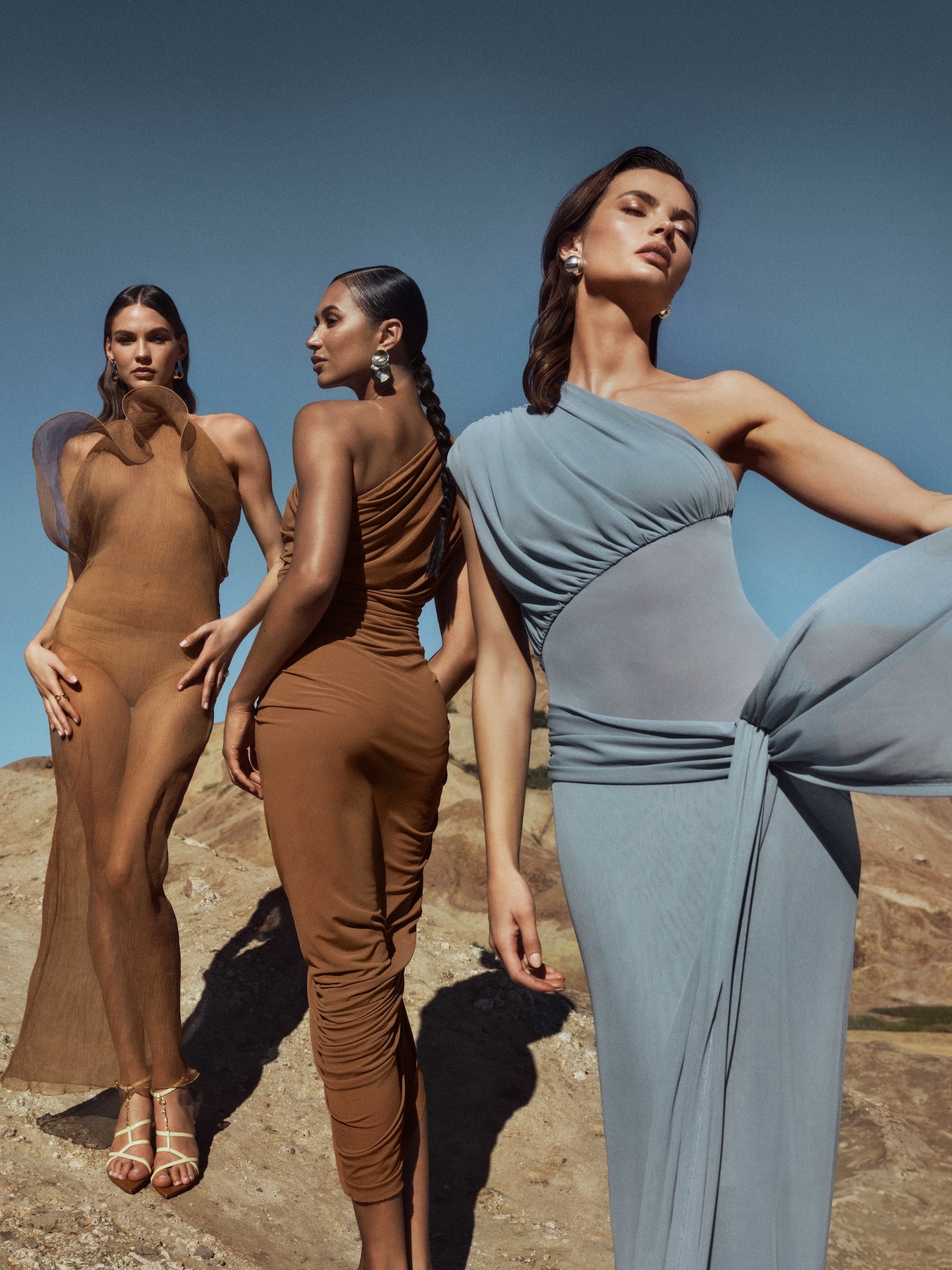 Three women in elegant dresses against a desert backdrop